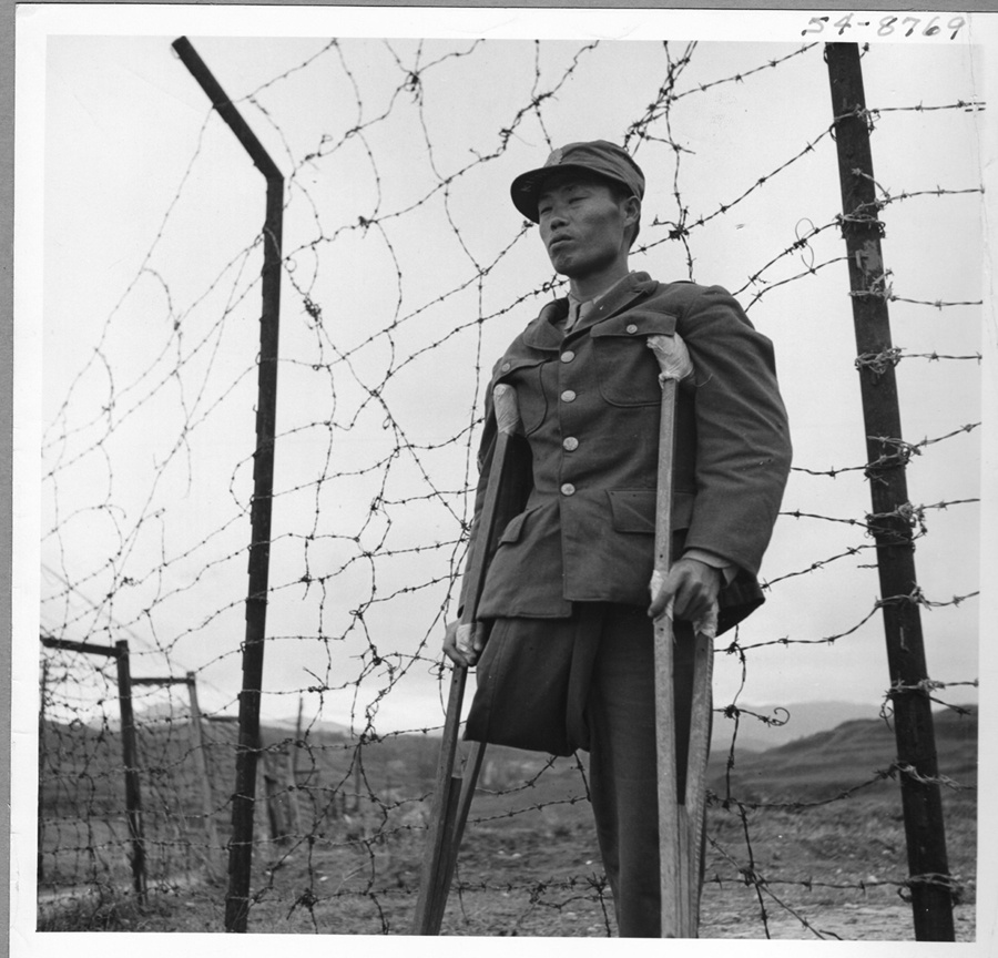  1950.10. 옹진전투에서 한쪽 다리를 잃은 한 국군 특무상사가 목발을 짚은 채 침통한 표정으로 철조망 앞에 서 있다.