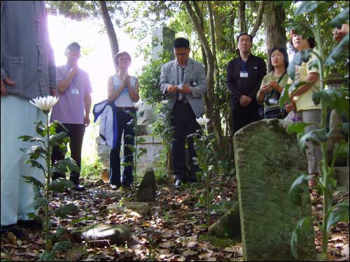 勝手に捨てられた朝鮮人強制徴用労働者の墓。 その場に菊の花を挿して涙の歴史を聞く韓国原爆2世患友会のメンバーと平和紀行参加者。