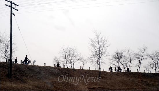 자전거를 탄 여러명의 북한 주민들이 줄지어 언덕길을 지나가고 있다.
