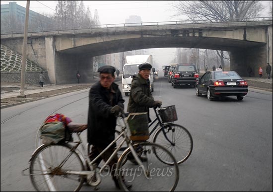 북한 주민들이 자전거를 끌고 도로를 건너고 있다.