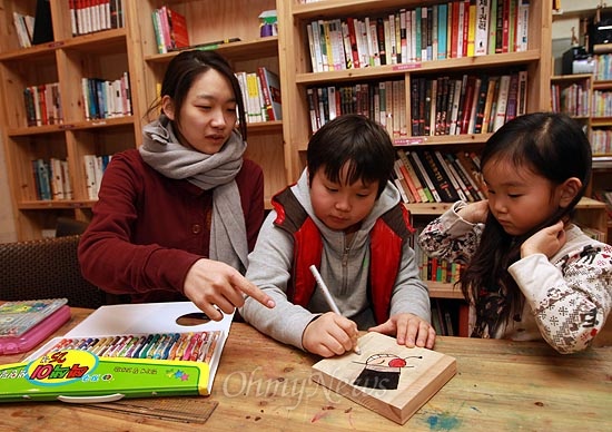 25일 오후 서울 용산구 효창운동장 인근 어린이 도서관 '고래이야기'에서 자원봉사로 온 장소원씨가 나무 조각에 그림을 그리는 방법을 아이들에게 가르쳐 주고 있다.