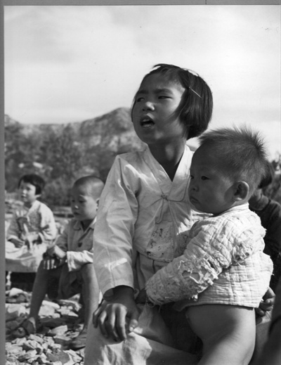  1950.10. 서울 은평. 한 소녀가 동생을 돌보며 불타버린 야외교실에서 수업을 받고 있다.
