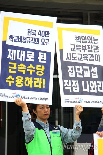 한 학교비정규직 노동자가 '근속수당 수용'이라 적힌 손팻말을 들고 서 있다. 