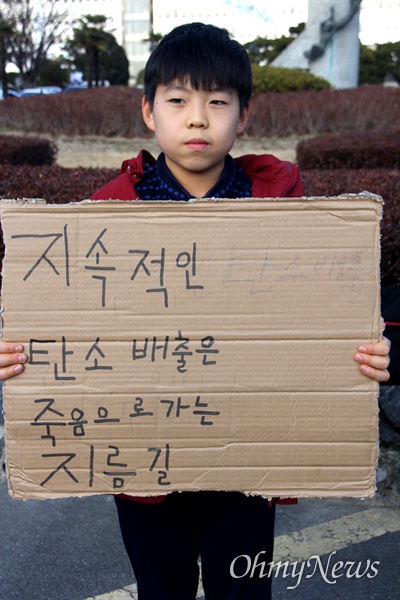 박지호 군이 2020년 11월 15일, '기후위기'를 알리기 위해 폐상자에 "지속적인 탄소 배출은 죽음으로 가는 지름길"이라고 쓴 손팻말을 들고 경남도청 정문 앞에 서 있다.