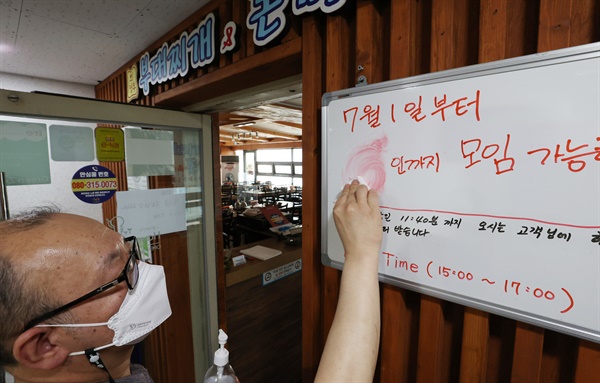 30일 오후 서울 한 음식점 관계자가 '다음달부터 6인까지 모임 가능' 안내 문구를 '4인까지 모임 가능'으로 수정하고 있다.