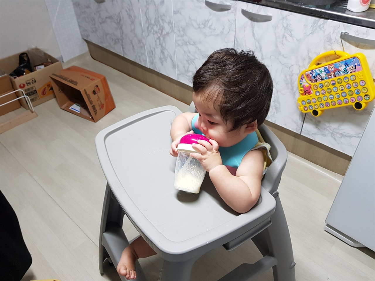 빨대 컵으로 앉아서 우유를 먹는 아기 
