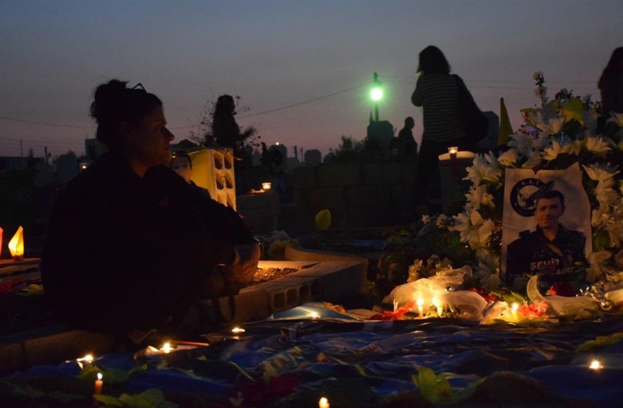 해 질 녘, 순교자 묘지를 찾은 어머니가 아들의 묘 비석 앞에 촛불과 꽃으로 장식해 놓은 아들 사진을 바라보며 앉아 있다. 