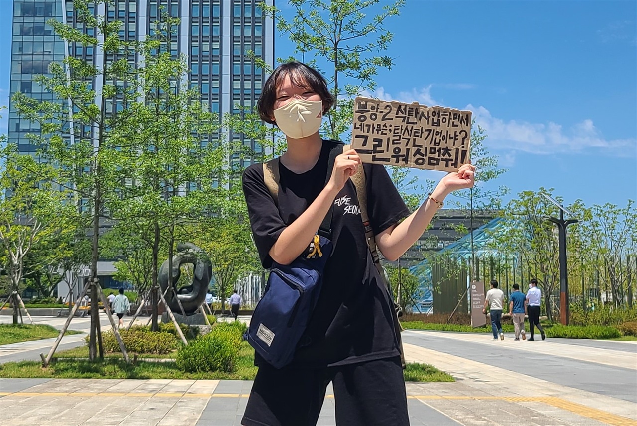 달복 작가가 전남 나주 한국전력 본사 앞에서 "그린워싱 멈춰!"라는 내용이 새겨진 피켓을 들고 있다.