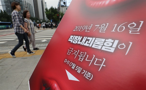 2019년 7월 16일 '직장 내 괴롭힘 금지법'이 시행된 이날 서울 광화문광장에서 직장갑질119 관계자들이 설치한 관련 안내판 뒤로 시민들이 지나가고 있다. 
