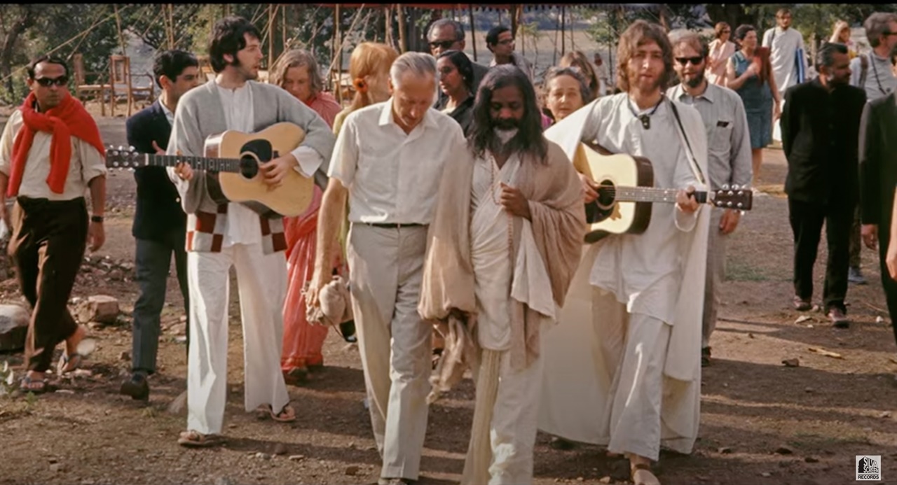  2021년에 개봉된 다큐멘터리 영화 <더 비틀스 앤 인디아> 공식 트레일러 캡처. 존 레논(왼쪽)과 폴 매카트니(오른쪽)가 기타를 연주하며 마하리시 마헤시 요기(가운데)를 따라 걷고 있다. 