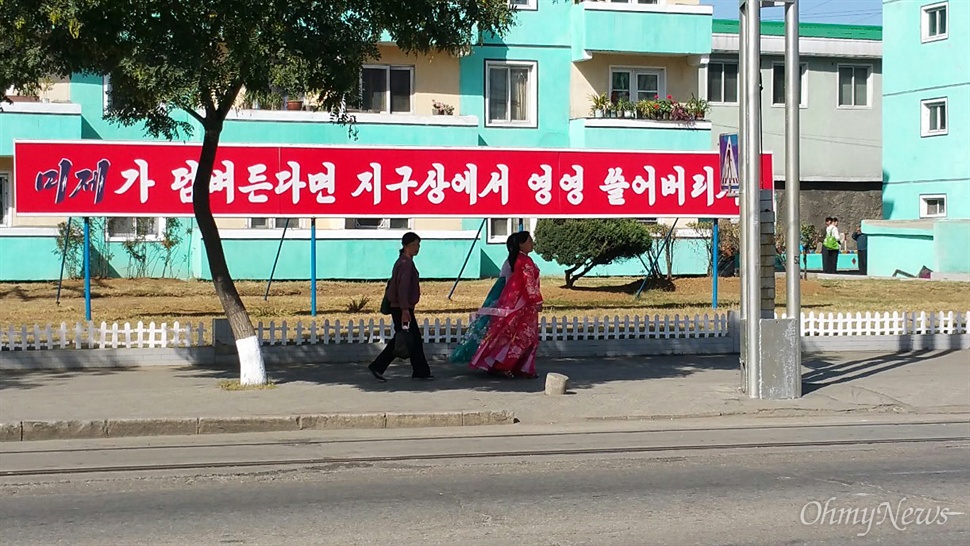  9일 낮 평양의 길거리. '미제가 덤벼든다면 지구상에서 영영 쓸어버리자'라는 문구 앞으로 한복을 입은 여성들이 지나가고 있다.