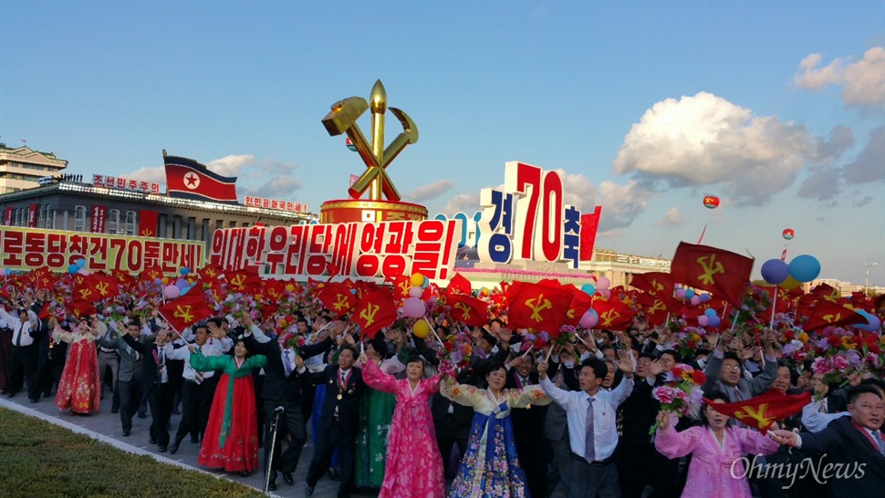  조선노동당 창건 70년 기념 열병식 현장. '위대한 우리 당에 영광을'이라는 문구 아래 북한 인민들이 손에 꽃을 들고 행진하고 있다.