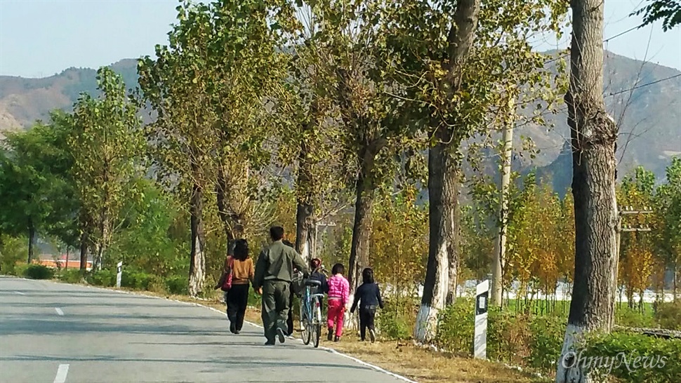  북한 자강도의 한 농촌 풍경. 성인 세 명과 어린이 세 명이 길을 걷고 있다. 