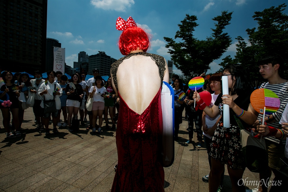  뙤약볕이 내리 쬐던 6월 28일, 서울 도심 한 복판에서 퀴어문화축제가 열렸다. LGBT참가자 뿐만 아니라 일반인들도 페스티벌과 행진에 참가했고 바로 옆에선 반대 집회도 열렸다.등이 파인 드레를 입은 트렌스젠더 여성이 자신이 준비한 프로그램의 사회를 보고 있다.