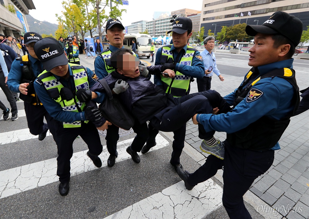 사지 들려 끌려나오는 시민 경찰 물대포에 맞아 사망한 고 백남기 농민 유가족과 백남기투쟁본부 회원들이 21일 오전 ‘제71주년 경찰의 날 기념식’이 열리는 세종문화회관앞에서 ‘대통령 사죄, 경찰청장 사퇴, 살인 경찰의 날 기자회견’을 개최하려 하자, 경찰들이 자리를 차지한 채 기자회견을 못하게 막았다. 기자회견에 참석하려는 한 시민을 경찰이 사지를 들어 끌어내고 있다.