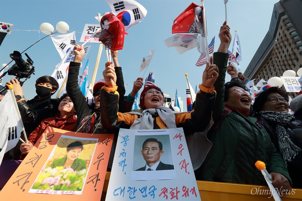 박정희-박근혜 사진 목에 건 지지자들 4일 오후 서울 덕수궁 대한문앞과 서울광장에서 박사모 등이 참여한 '탄핵기각을 위한 국민총궐기 운동본부’(탄기국) 주최 제16차 박근혜 대통령 탄핵기각 대규모 집회가 열렸다. 박정희, 박근혜 사진을 목에 건 참가자들이 태극기와 성조기를 흔들고 있다.