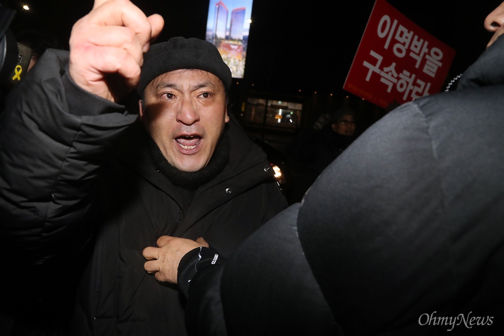 바깥으로 밀려난 'MB 구속' 시위대 이명박 전 대통령이 트리플데이를 앞두고 18일 오후 서울 강남구 신사동의 한 식당에서 친이계 전·현직 수석 및 의원들과 송년 회동을 위해 도착하자, "이명박 구속"을 외치는 시위대가 경호원들에 둘러싸여 식당 바깥으로 밀려나고 있다. 