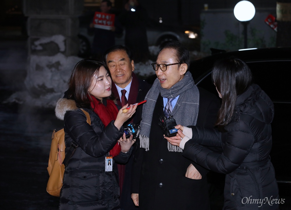  이명박 전 대통령이 트리플데이를 앞두고 18일 오후 서울 강남구 신사동의 한 식당에서 친이계 전·현직 수석 및 의원들과 송년 회동을 위해 들어서다 취재진의 질문을 받고 있다. 왼쪽 뒤는 이재오 늘푸른한국당 대표. 더 뒤편에는 "이명박을 구속하라" 피켓을 든 시위대도 보인다.  