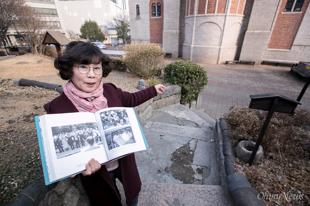  유시춘 작가가 6.10항쟁 당시 올라갔던 서울 중구 정동 대한성공회 주교좌성당 종탑 앞 마당에 당시 사진을 들고 섰다.