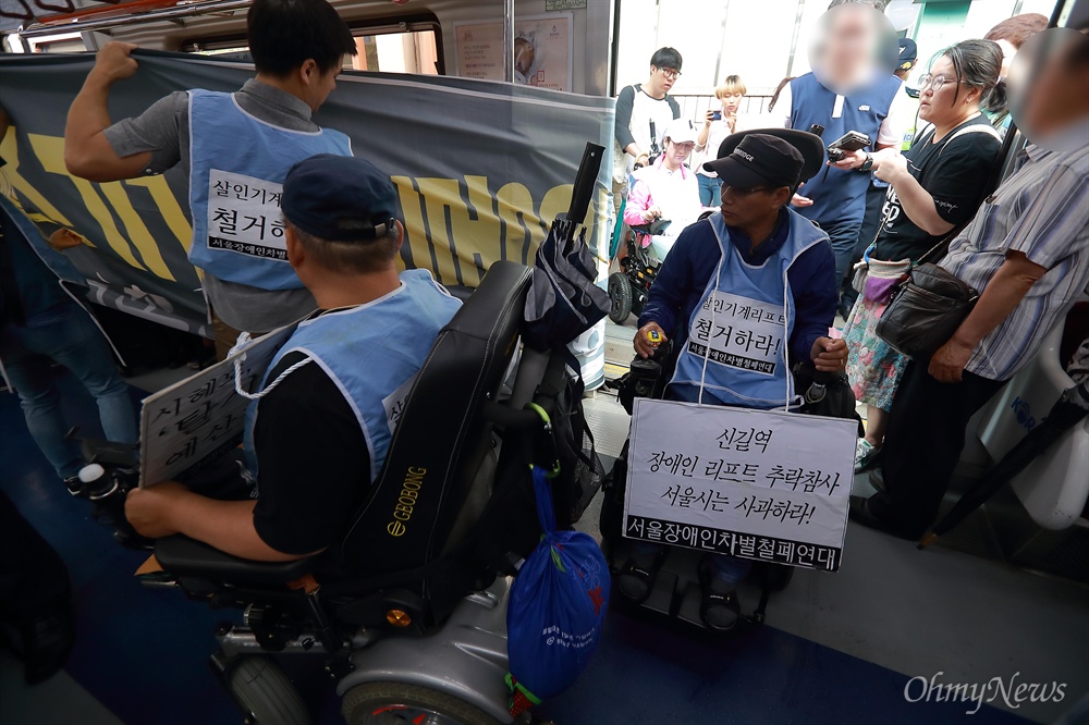  목에 요구사항이 적힌 피켓을 건 휠체어 장애인들이 지하철에 줄지어 탑승하고 있다.