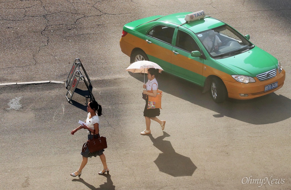뜨거운 아침 햇살 피하는 평양 여성 4일 오전 평양 남북통일농구경기 취재차 방북한 사진기자 카메라에 양산으로 뜨거운 아침 햇살을 피하는 여성, 손님을 태우고 가는 택시의 모습이 담겼다.