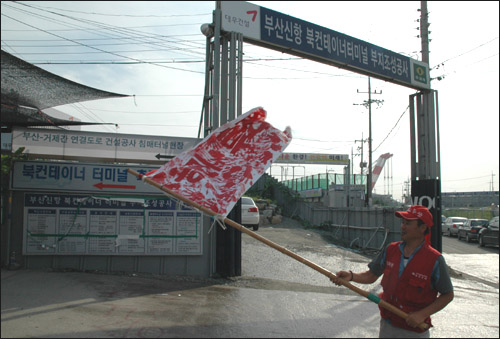 한 덤프 노동자가 부산신항 북컨테이너터미널 부지조성공사장 입구 앞에서 손도장을 찍은 깃발을 흔들고 있다.