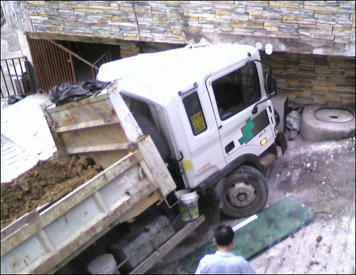 무리하게 진입을 시도하다 삼안빌라를 들이받은 덤프트럭, 이로 인해 빌라 외벽이 손상되고 유리창과 도시가스관이 파열됐다.