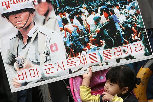 민주화 운동을 하다 한국에 온 부모를 둔 어린이가 군사독재 정권을 규탄하는 피켓을 쳐다보고 있다.