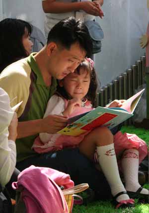 아빠 무릎에 앉아 책을 보는 어린이