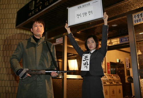 영화 <바르게 살자> 중 은행 강도 역을 맡은 배우 정재영이 은행 직원(이영은)을 총으로 겨누고 잇다.