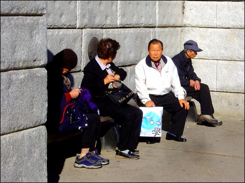 따스한 햇볕이 그리운 계절, 청계천의 돌담 양지바른 곳에 사람들이 한가로이 앉아 쉬고 있다.