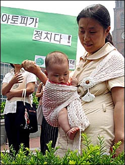  '아토피가 정치다'는 구호가 내걸린 초록정치연대의 행사장에 아기를 안은 한 엄마가 나와있다.