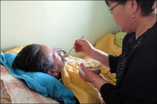 지난해 11월 21일 한 노인돌보미가 노환으로 거동이 불편한 한 할머니에게 배즙을 갈아 먹이고 있다. 그는 4명의 노인을 돌보고 있다.