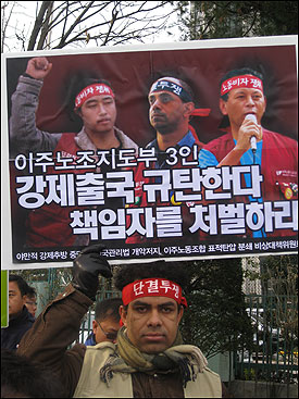 한 이주노동자가 18일 오전 서울 세종로 정부종합청사 앞에서 열린 기자회견에서 '이주노조지도부 3인 강제출국 규탄한다, 책임자를 처벌하라'고 쓰인 팻말을 들고 있다.