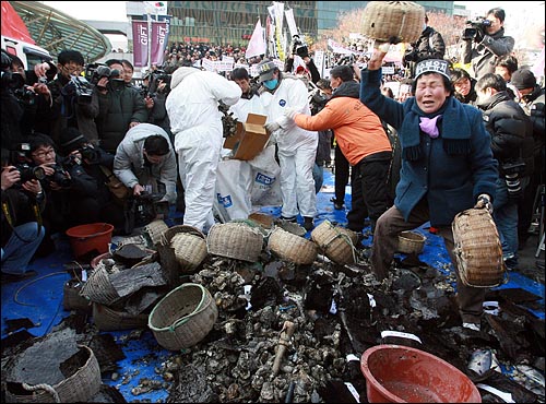 서울역 광장에 모인 기름유출 피해 어민들이 기름에 오염된 김, 생선, 굴 등을 쌓아 놓고 어구를 던지며 오열하고 있다.