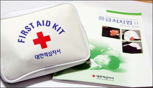  응급구조법 교재로 쓰이는 책(응급처치법)과 응급구조키트(First Aid Kit). 응급구조키트 안에는 삼각건, 압박붕대 등이 들어있다.