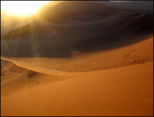 사막의 일몰. 태양은 붉은 노을로 붉은 사막을 검게 태우며 서쪽 끝으로 향하고 있다.