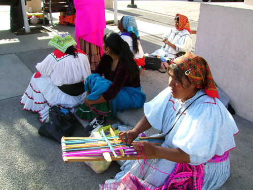 전통 복장을 한 채 길 가에 앉아 옷감을 짜고 있다.