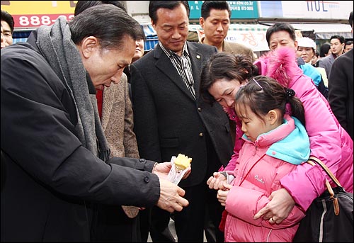 3일 오후 서울 관악구 봉천11동 원당시장을 방문한 이명박 당선인이 시장상인에게 산 떡을 한 어린이에게 나눠주고 있다.