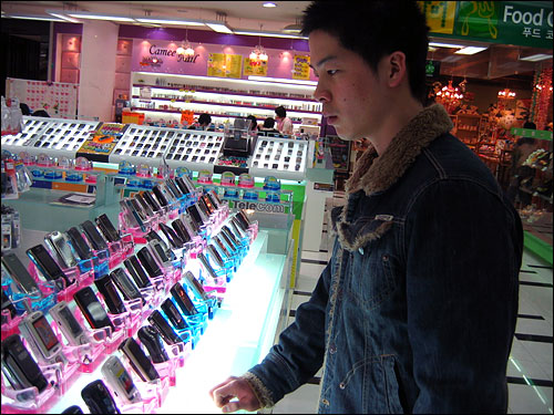 수 많은 제품들이 진열되어 있는 휴대폰 가게. 그 앞에서 휴대폰을 고르고 있는 동생