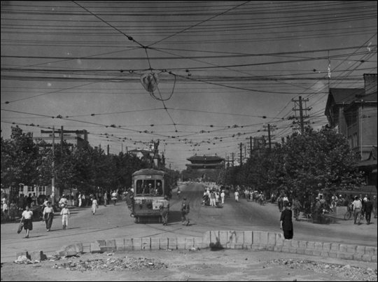 1945년 9월 11일, 35년간의 일제 강점기를 끝낸 서울 역 앞 풍경으로 멀리 숭례문이 보인다. 그 시절에는 지상 전차가 중요 교통 수단으로 전차에 전기를 공급한 전선이 도로 위에 거미줄처럼 널려 있었다.