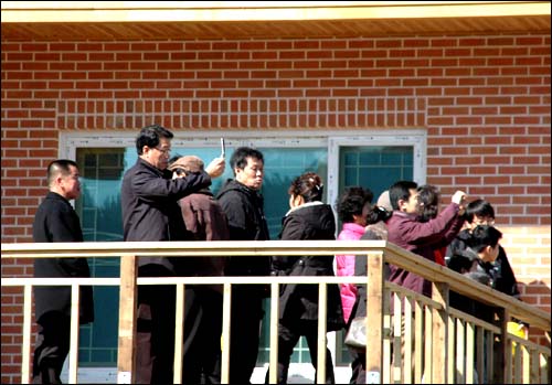 관광객들이 노무현 대통령의 사저 옆에 있는 마을이장 집에 올라가 사저를 보며 휴대전화에 담고 있다.