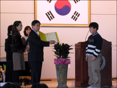 학교에서 준비한 선물 두마초 이강문 교장이 학교에서 제작한 영상물 CD와 추억의 앨범 등이 수록된 기념품을 졸업생들에게 전달하고 있다.