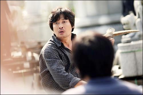 영화 <추격자>에서 전직 경찰이자 보도방 업주인 엄중호(김윤석)가 곡괭이를 들고 길을 막는 경찰을 위협하고 있다.