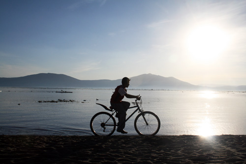 햇살이 퍼지는 호수를 배경으로 자전거를 타는 소년.