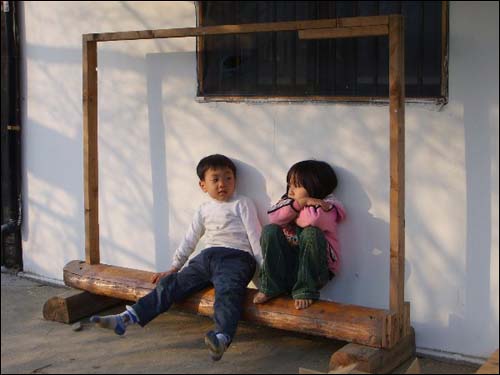 햇살이 따스한 어린이집 벽면 나무의자에 기대고 앉아 눈빛으로 우정을 나누는 꼬마친구들
