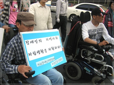한 장애인이 장애인의 권리를 이야기하는 피켓을 들고 행진을 하고 있다. 