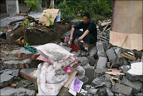 파괴된 집에서 간신히 베게와 이불을 꺼낸 한 남자가 넋이 나간 채 앉아있다.
