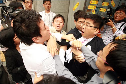 항의스티커를 조선일보 게시판에 붙이는 과정에서 스티커를 떼어내는 조선일보 직원과 기자회견 참가자가 몸싸움을 벌이고 있다.