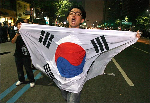 한미 쇠고기 협상 장관 고시 무효를 주장하며 30일 새벽까지 서울 세종로 네거리 도로에거 밤샘농성을 벌이던 시민, 학생들을 경찰이 강제해산시키자 한 참가자가 태극기를 펼쳐들고 도로에서 항의시위를 벌이고 있다,